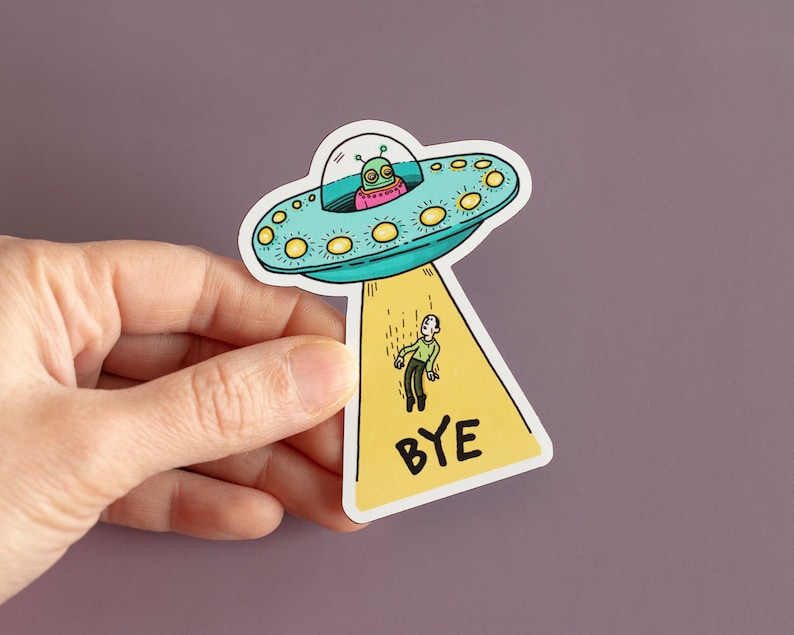 May include: A yellow and blue sticker with a cartoon alien spaceship and a person falling from it. The sticker says "BYE" in black letters.