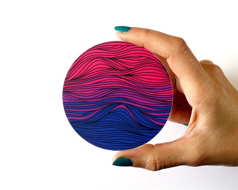May include: A round sticker with a wavy, abstract design in pink, purple, and blue colors. The sticker is being held by a hand.