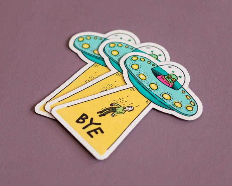 May include: Three yellow and blue alien spaceship stickers with a person falling from the top one. The bottom sticker says "BYE" in black letters.