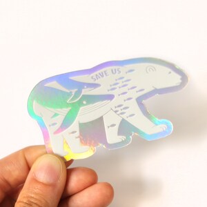 May include: A holographic sticker featuring a polar bear carrying a whale and a smaller dolphin. The sticker has the text "SAVE US" and a school of fish swimming around the animals.