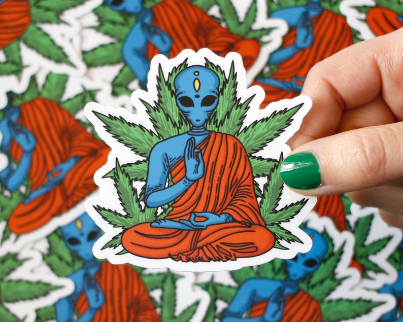 May include: A blue alien meditating in a red robe surrounded by green marijuana leaves. The alien has a third eye and is sitting in a lotus position.