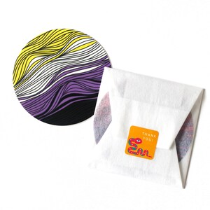 May include: A round coaster with a purple, white, and yellow striped design. The coaster is on a white surface with a small orange square sticker that says "Thank You!" with a red snake illustration.