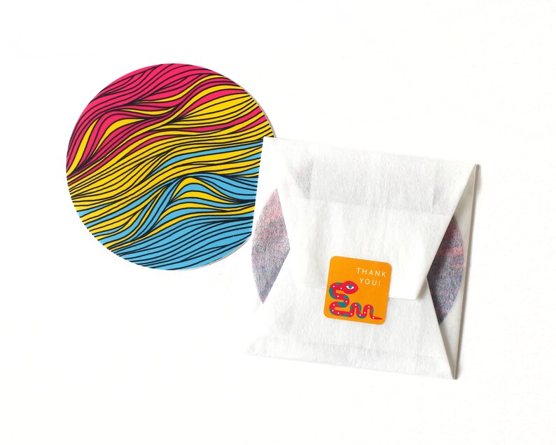 May include: A round sticker with a colorful wavy pattern in pink, yellow, and blue. The sticker is on a white background. A smaller sticker with a snake design and the text "Thank You!" is also visible.
