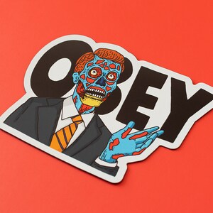 May include: A black and white sticker with the word "OBEY" in large, bold letters. A cartoon image of a man with blue and red skin, wearing a suit and tie, is partially visible behind the word "OBEY".