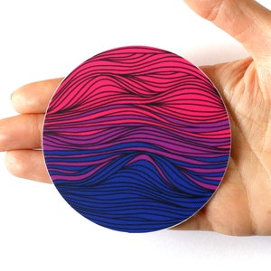 May include: A round sticker with a wavy, abstract design in pink, purple, and blue colors. The sticker is in the shape of a circle and has a glossy finish.