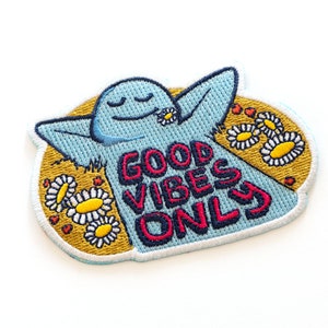 May include: A blue embroidered patch with a cartoon character with arms raised and the text "GOOD VIBES ONLY" in red and blue lettering. The character is surrounded by yellow daisies.