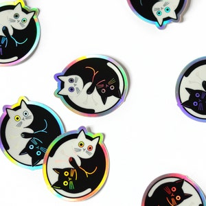May include: A set of eight iridescent stickers featuring a yin yang design with two cats facing each other. The cats are black and white and have different colored eyes.