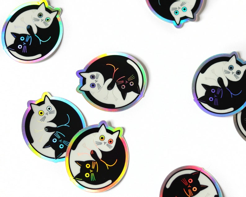 May include: A set of eight iridescent stickers featuring a yin yang design with two cats facing each other. The cats are black and white and have different colored eyes.