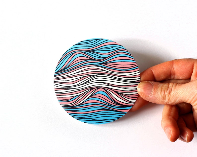 May include: A round sticker with a wavy pattern in blue, pink, and white colors. The waves are outlined in black.