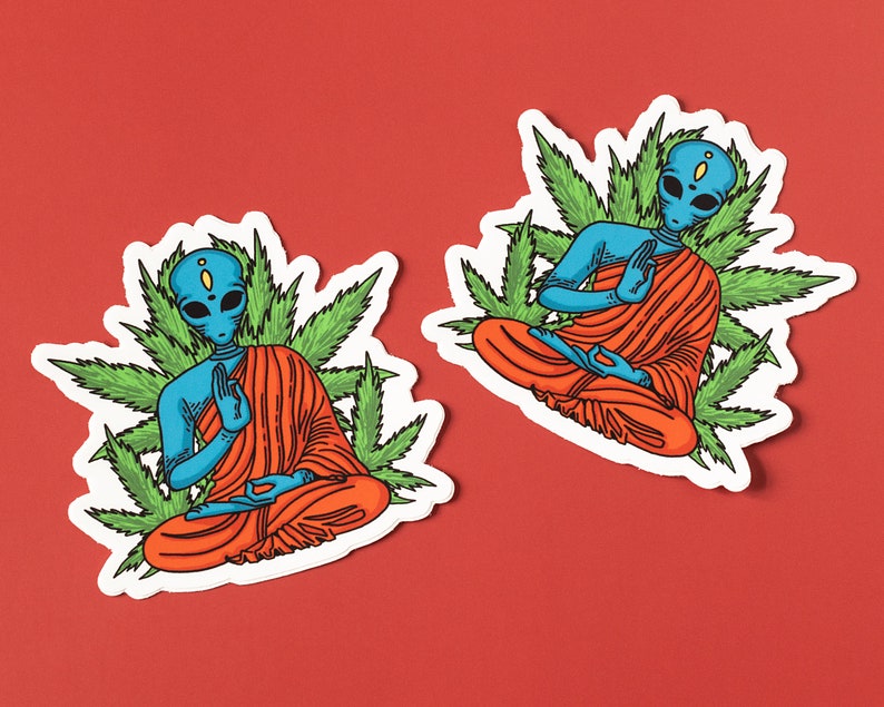 May include: Two blue alien figures in orange robes meditating in a lotus position surrounded by green marijuana leaves. The aliens have large eyes and are sitting on a white background.