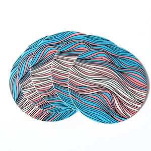 May include: Four round coasters with a wavy pattern in blue, pink, and white. The coasters are stacked on top of each other.