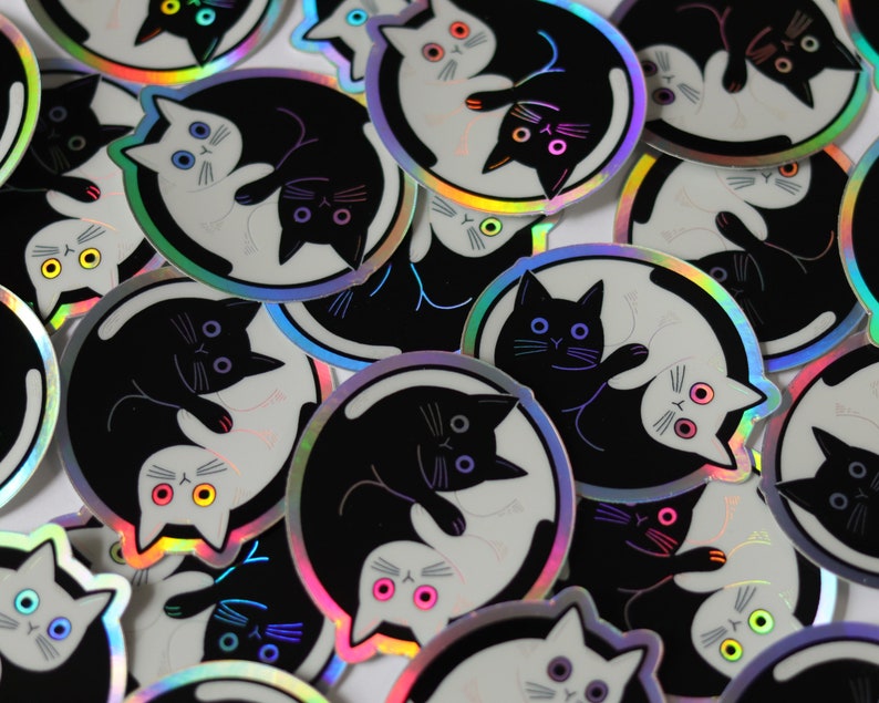 May include: A collection of iridescent stickers featuring black and white cats in a yin yang design. The stickers have a holographic finish and are perfect for adding a touch of whimsy to laptops, water bottles, or journals.