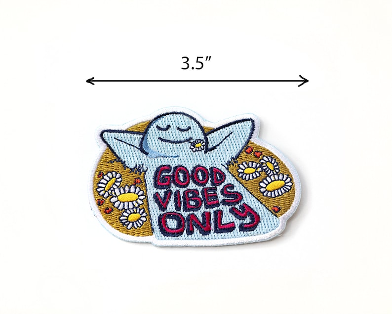 K&ouml;nnte beinhalten: Gestickter B&uuml;gel-Patch mit einer blauen Comicfigur mit dem Text "Good Vibes Only" umgeben von gelben G&auml;nsebl&uuml;mchen. Der Patch hat einen Durchmesser von 8,9 cm.