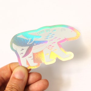 May include: A holographic sticker featuring a polar bear with a whale swimming inside it. The sticker has the text "Save Us" on it and is surrounded by a school of fish.