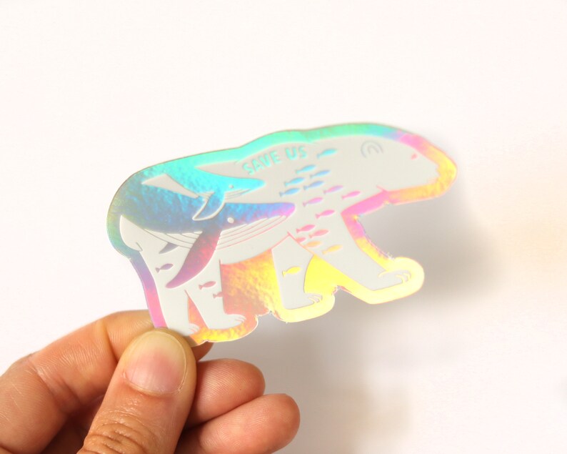 May include: A holographic sticker featuring a polar bear with a whale swimming inside it. The sticker has the text "Save Us" on it and is surrounded by a school of fish.