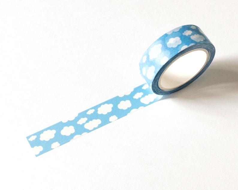 May include: A roll of blue washi tape with a repeating pattern of white clouds. The tape is partially unrolled, revealing the cloud design. The tape is on a white background.