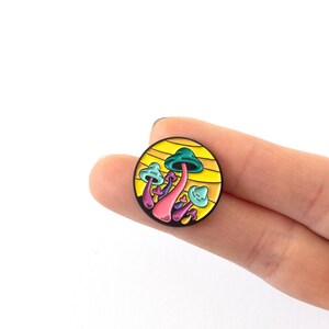 May include: A colorful enamel pin featuring a cluster of mushrooms with a yellow background. The mushrooms are pink, purple, blue, and green.
