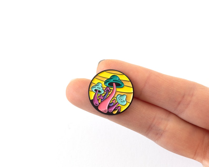 May include: A colorful enamel pin featuring a cluster of mushrooms with a yellow background. The mushrooms are pink, purple, blue, and green.