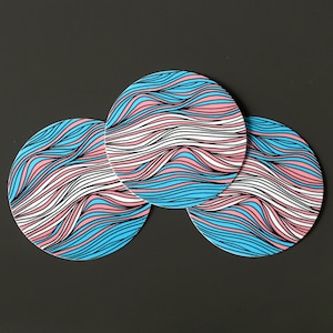 May include: Three round coasters with a wavy, abstract design in shades of blue, pink, and white.