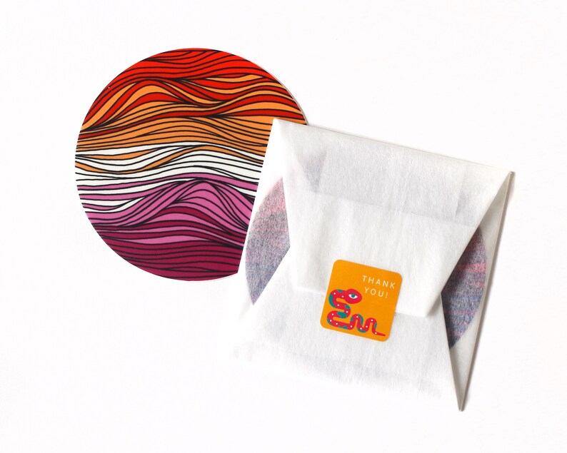 May include: A round sticker with a colorful design of wavy lines in red, orange, pink, and white. The sticker is packaged in a white envelope with a small orange sticker that says "Thank You!" and features a red, green, and blue snake design.