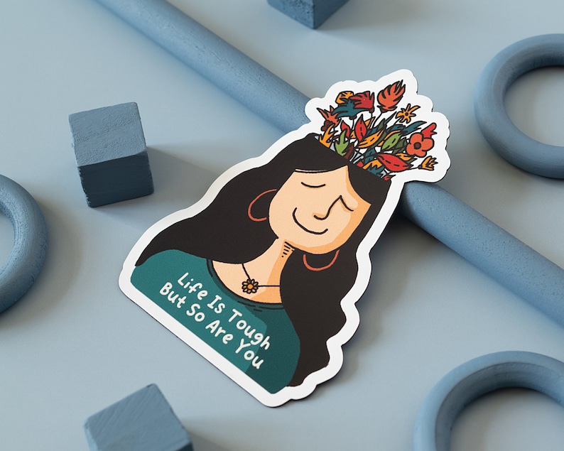 May include: A sticker featuring a cartoon illustration of a person with long black hair and flowers growing out of their head. The person is smiling and the text "Life is Tough But So Are You" is written on the sticker.