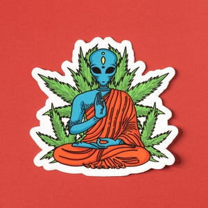 May include: A blue alien meditating in a red robe, surrounded by green marijuana leaves. The alien has a third eye and is in a peaceful pose.