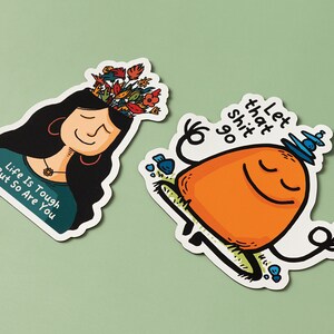 May include: Two colorful stickers with motivational messages. The first sticker features a woman with flowers growing out of her head and the text "Life is tough but so are you". The second sticker features a cartoon orange character meditating with the text "Let that shit go".