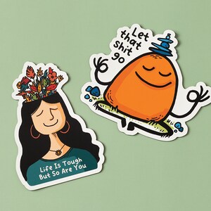 May include: Two colorful stickers with motivational messages. One sticker features a cartoon person with flowers growing out of their head and the text "Life is tough but so are you". The other sticker features a cartoon orange character meditating with the text "Let that shit go".