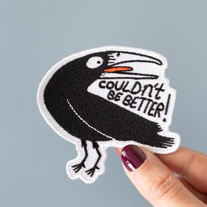 May include: White embroidered patch with a black bird with an open beak and the text "couldn't be better!" in black lettering.