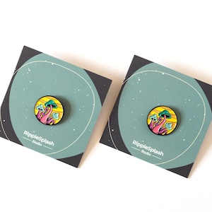 May include: Two enamel pins featuring a colorful mushroom design with a yellow and orange background. The pins are on a black and green background with the text "RippleSplash Studio" on each card.