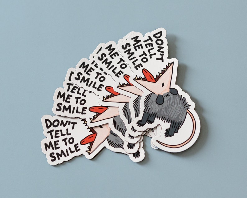 May include: A set of six stickers featuring a cartoon opossum with the text "Don't tell me to smile". The opossum is gray with a pink mouth and red tongue. The stickers are white with black text.