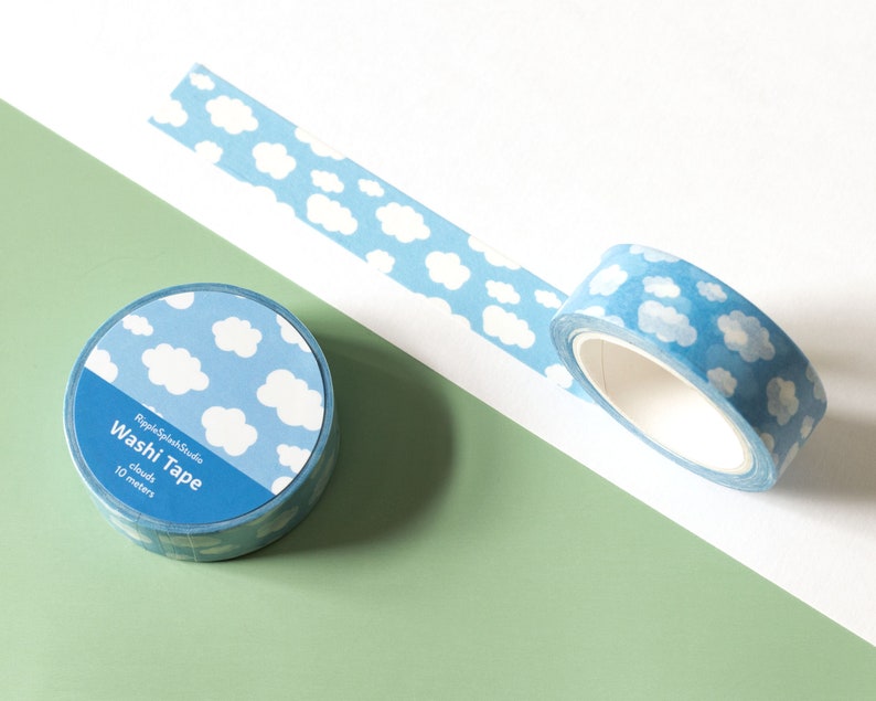 May include: Two rolls of washi tape with a sky-blue background and white cloud pattern. One roll is unrolled, revealing the tape's design. The text "RippleSplashStudio Washi Tape clouds 10 meters" is printed on the label.
