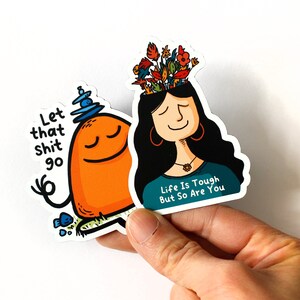 May include: Two colorful stickers with motivational messages. The first sticker features a cartoon character meditating with the text "Let that shit go". The second sticker features a cartoon woman with flowers on her head and the text "Life is tough but so are you".