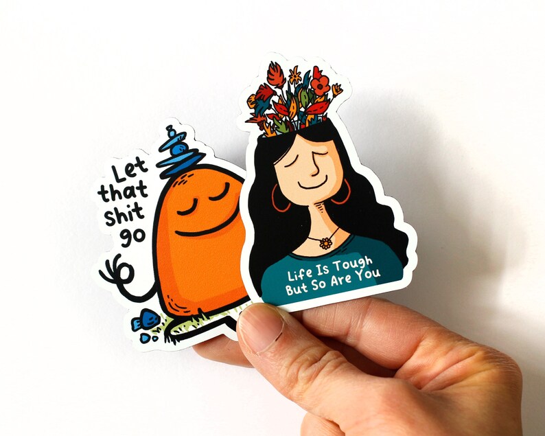 May include: Two colorful stickers with motivational messages. The first sticker features a cartoon character meditating with the text "Let that shit go". The second sticker features a cartoon woman with flowers on her head and the text "Life is tough but so are you".
