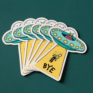 May include: A set of six colorful stickers featuring a cartoon alien in a flying saucer with the text "BYE" on a yellow background.