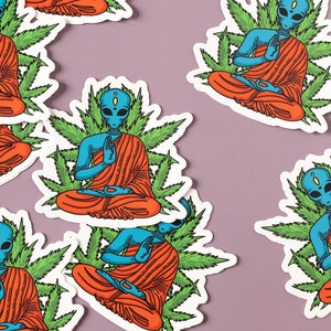May include: A set of six stickers featuring blue alien figures meditating in a lotus position surrounded by green marijuana leaves. The aliens are wearing orange robes and have a third eye on their foreheads.