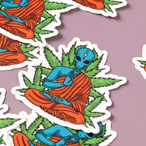 May include: A set of stickers featuring blue alien figures meditating in a lotus position surrounded by green marijuana leaves. The aliens are wearing orange robes.