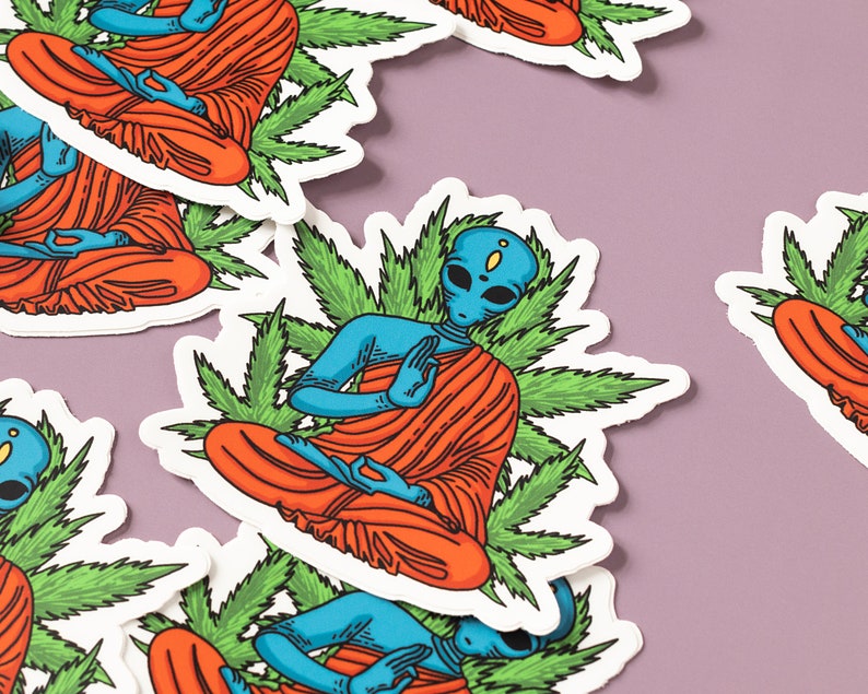 May include: A set of stickers featuring blue alien figures meditating in a lotus position surrounded by green marijuana leaves. The aliens are wearing orange robes.