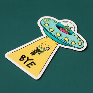 May include: A yellow sticker with the word "BYE" in black lettering. A cartoon alien in a flying saucer is leaving a person behind.
