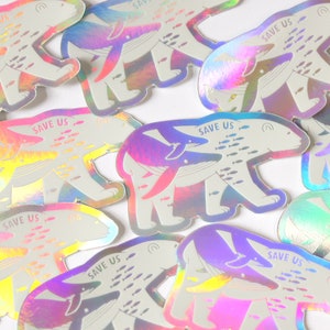 Op de afbeelding: Een verzameling regenboogkleurige stickers met een ijsbeer die een walvis en een school vissen draagt. De stickers hebben de tekst "Save Us" erop gedrukt.