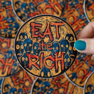 May include: A round sticker with a yellow and blue design. The sticker says "Eat the Rich" in red and black lettering.
