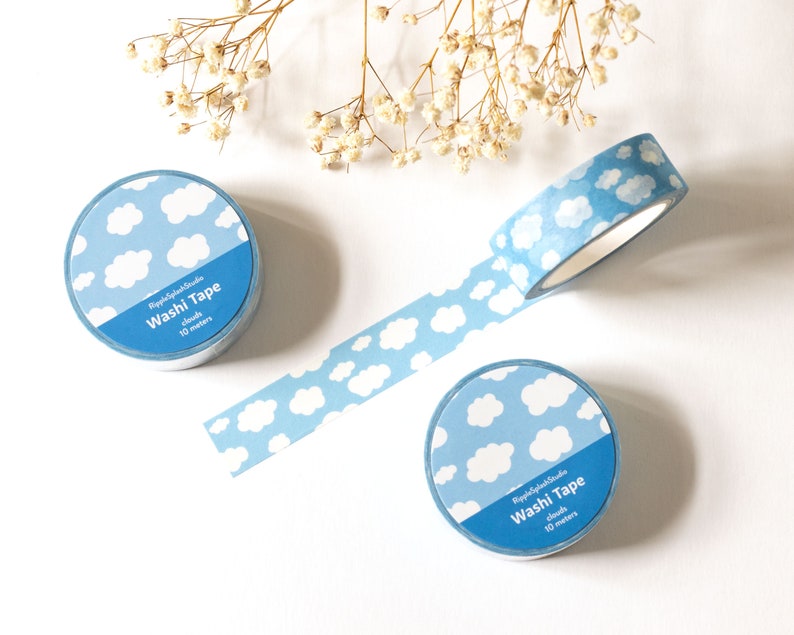 May include: Three rolls of washi tape with a blue and white cloud pattern. One roll is unrolled, showing the tape with the same cloud design. The text on the tape reads "RippleSplashStudio Washi Tape clouds 10 meters."