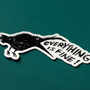 May include: A black and white sticker with a cartoon crow with its beak open and the text "EVERYTHING IS FINE!" printed on it. The sticker is on a teal background.