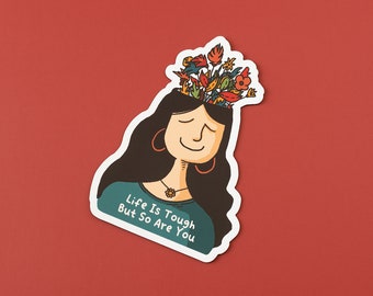 Pode incluir: Um adesivo com uma ilustração de desenho animado de uma mulher com flores crescendo de sua cabeça. O texto "Life Is Tough But So Are You" está escrito no adesivo.