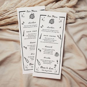 May include: Two white rectangular paper menus with black hand-drawn illustrations of a disco ball, stars, and food items. The text reads Our Menu, starter, main course, dessert, drinks, Eloise & Sam, and 19th August 2024, with listed food items.