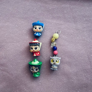 May include: Four small plastic figurines of cartoon characters wearing hats, a blue hat, a red hat, a green hat, and a gray owl figurine.