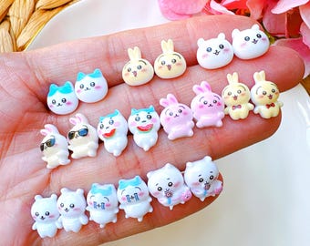 May include: A collection of small, colorful resin charms in various animal shapes, including bunnies, cats, and bears. Some charms have sunglasses, bow ties, or watermelon slices. The charms are white, pink, yellow, and blue.