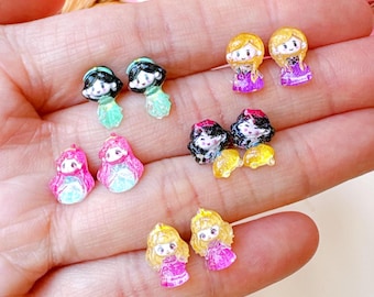 May include: A set of ten princess-themed earrings. The earrings are made of clear resin and feature various princesses in different colours, including pink, purple, green, and yellow.