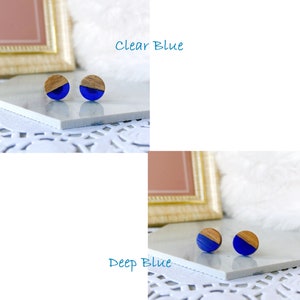 May include: Wooden stud earrings with a half-circle of vibrant blue resin. The earrings have a natural wood grain finish on the other half. The text "Clear Blue" and "Deep Blue" are visible in the image, indicating color options. These earrings are a simple, modern accessory.