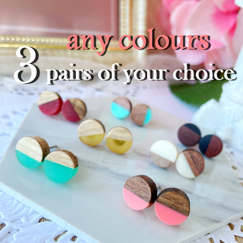 May include: A collection of wooden stud earrings in various colors, including red, teal, yellow, white, and pink. Each earring features a wooden half-circle design paired with a colored resin half-circle. Text reads: "any colours" and "3 pairs of your choice."